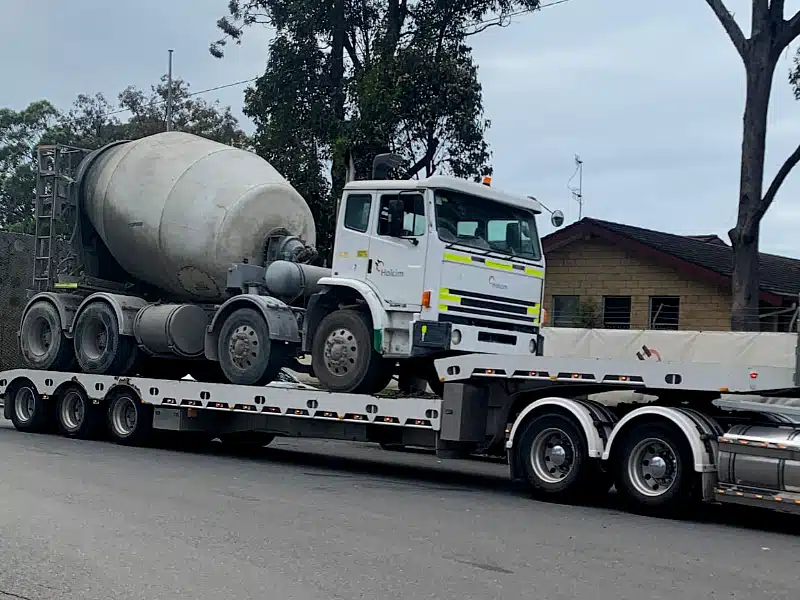 A cement truck being towed on an off set trailer