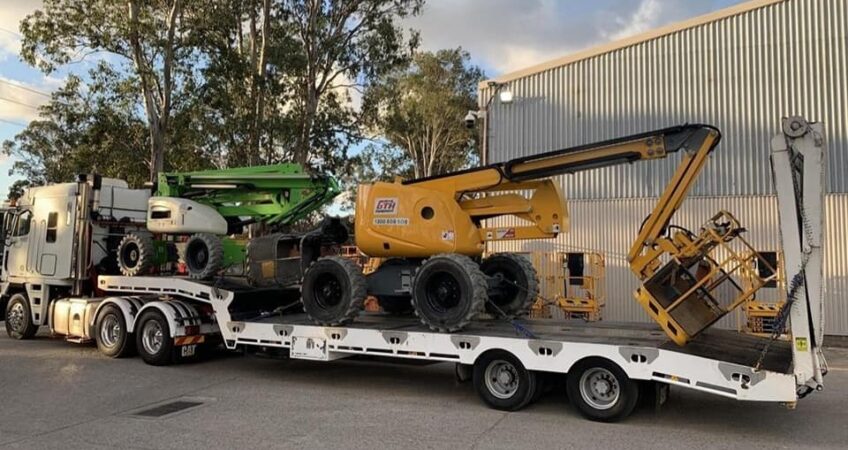 2 cherry pickers or boom lifts being transported on a low bed trailer