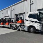 5 forklifts on a flatbed trailer being towed