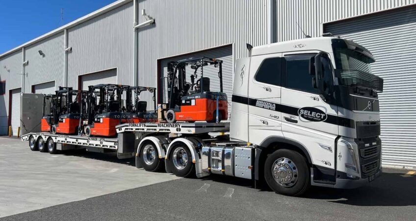 5 forklifts on a flatbed trailer being towed by a prime mover as part of Select Till Tray's heavy machinery Sydney towing