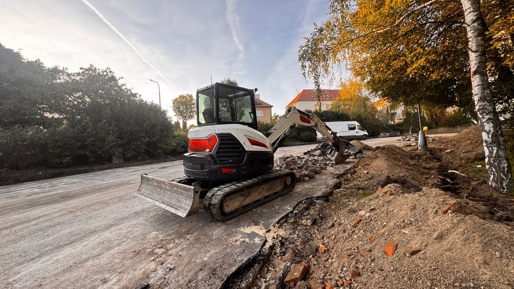 Compact bobcat excavator breaking asphalt at a construction site.