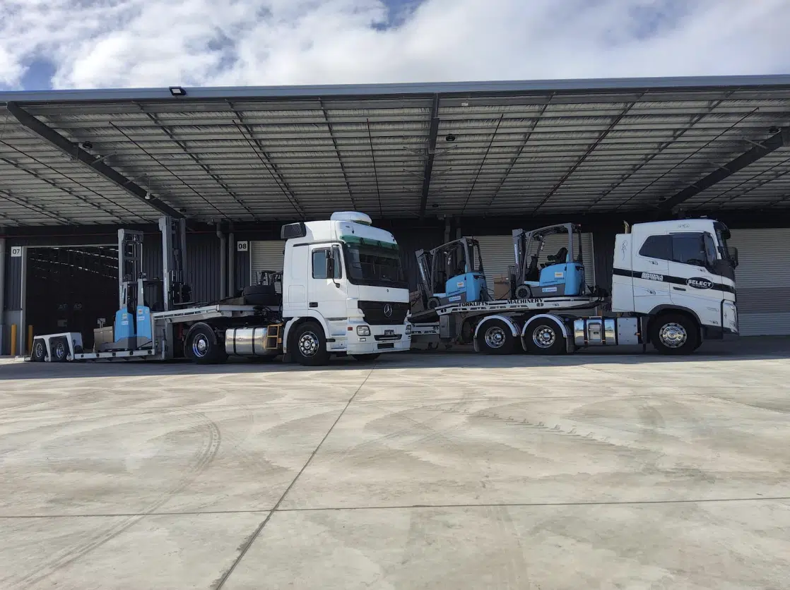 Forklifts loaded onto tilt tray trucks for transport.