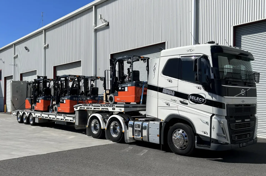 Forklifts secured on the back of a tow truck.